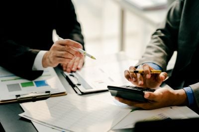 Two business professionals reviewing financial documents and charts while using a calculator.