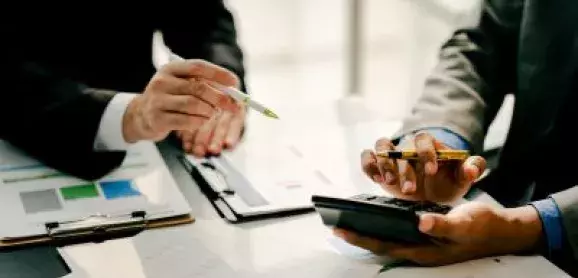 Two business professionals reviewing financial documents and charts while using a calculator.